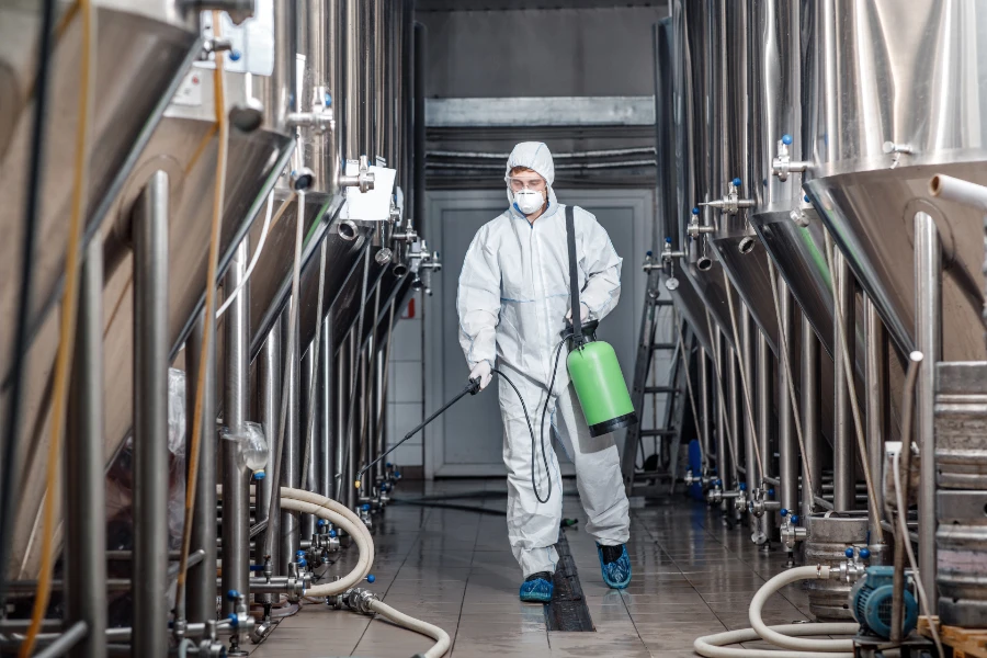 Man in safety gear, with spray cleaner in factory.